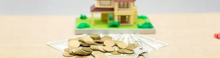 מטבעות ושטרות כסף מונחים על השולחן עם מפתח וברקע הדמיה של בית עם חצר